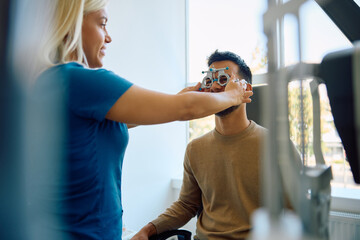 Female optometrist using optical trial frame during patient's eyesight exam.