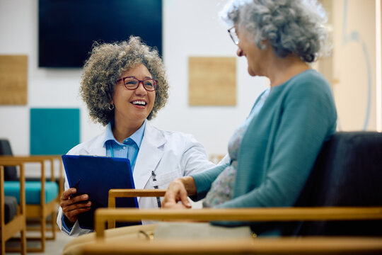 Happy female doctor communicating with senior woman at medical clinic.