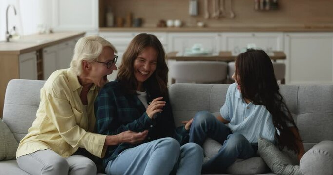 Excited happy grandma, young mother and kid tickling each other, shouting, playing active games on home sofa, having fun together, laughing, enjoying playtime, leisure