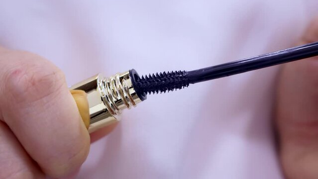 Black mascara brush applicator with the tube in woman hands close up