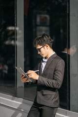 Asian male businessman use smartphone and holding laptop computer, Walk enjoy smiling while doing commuting at business center.