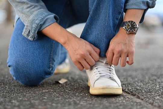 Close-up image of an Asian young man sitting on the footpath and tying shoelaces, A Man traveling in the city, Solo traveling concept