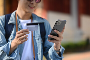 A Close-up of an Asian tourist holding a credit card and smartphone for cashless payment online for...