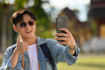 Close-up image of Asian tourist with thumb up to introduce tourist attractions to viewers who watch a live broadcast on the phone
