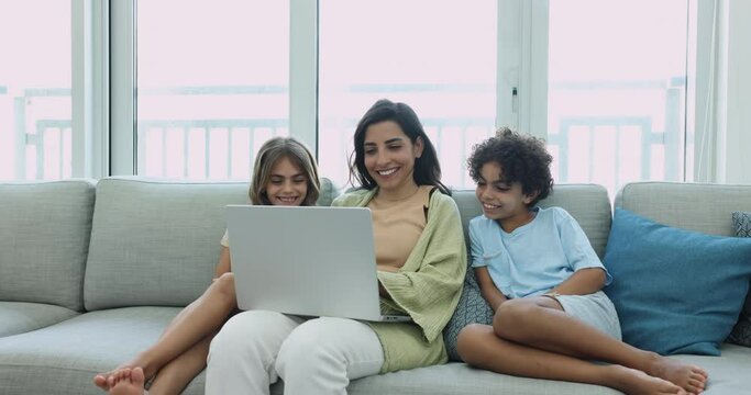 Happy Latin mother and preteen son and daughter children resting on sofa with laptop, using ecommerce application for shopping, media service, browsing Internet, enjoying leisure, communication