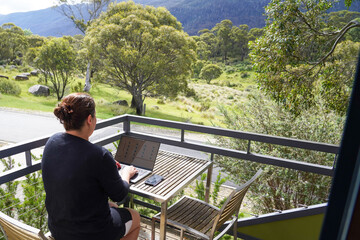 A woman working remotely from her balcony looking over bushland and mountains