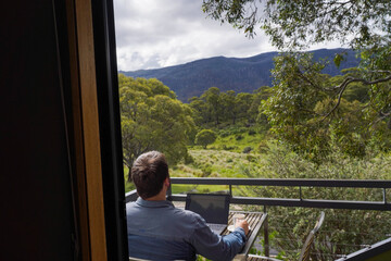 Fototapeta premium A man working remotely from his balcony looking over bushland and mountains