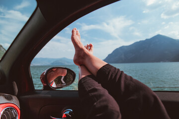 Bare feet of a girl placed outside the window of a moving car during a summer vacation trip. in the...