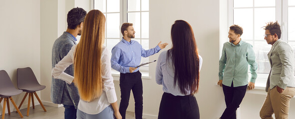 Modern business coach or team manager meeting with a group of diverse people in the office. Male business professional with a clipboard talking to a team of young multiracial people. Banner background - obrazy, fototapety, plakaty
