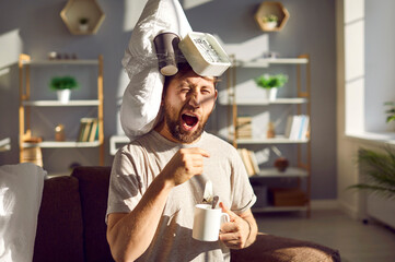Funny guy can't wake up early in the morning. Young man with a pillow, coffee cup and alarm clock...