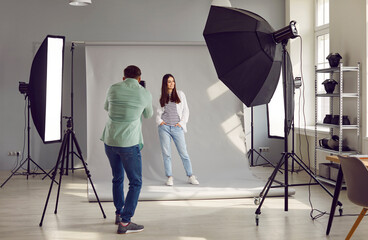 Beautiful model posing for male photographer in studio. Rare view of photographer taking pictures of female model with digital camera in photo studio with professional photographic equipment - Powered by Adobe