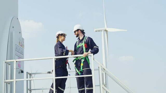 Professional technician mand and woman workers stand and discuss about work and stay in base of windmill or wind turbine in area of green power plant.