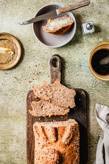 Vollkornbrot auf einem Holz Schneidebrett und eine Tasse Kaffee auf einem grünen Tisch. Draufsicht.