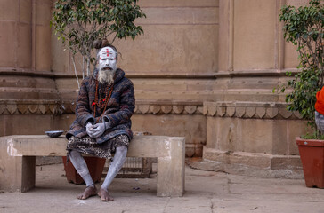 Fototapeta na wymiar Portrait of an old holy sadhu baba with ash on his face sitting on ghats near river ganges. 