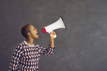 Noisy millennial gen z African American girl on black studio background yell shout of good sale deal or discount. Loud mad angry ethnic woman hold speaker make announcement. Attention concept. - obrazy, fototapety, plakaty
