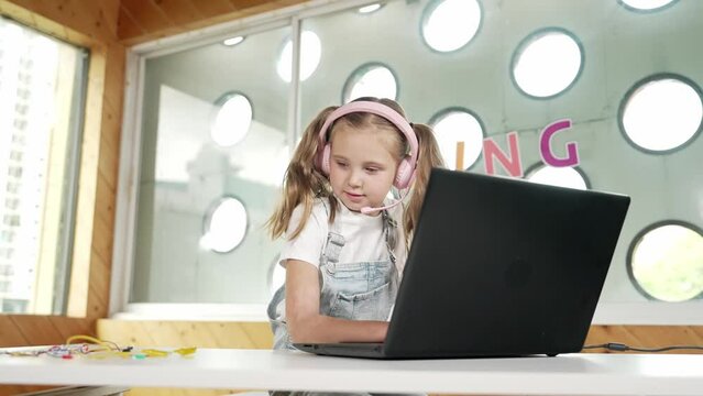 Caucasian girl wearing headphone and looking at laptop while study mechanics. Skilled student working by using laptop to searching and learning electric equipment on table. Smart classroom. Erudition.