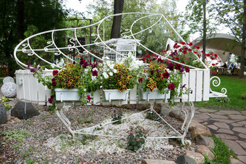 In the garden there is a flowerbed with a white grand piano made of both fittings and wooden slats...