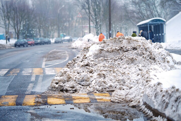 Pile of snow collected on roadside in the city by snowplow machine and utility workers. Stuck of...