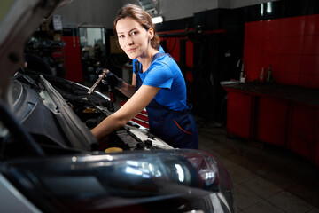 Young woman works under the open hood of a car