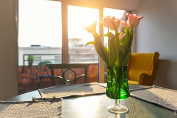 Beautiful fresh pink tulips bouquet in green glass vase on table in warm sunset sun lights against...