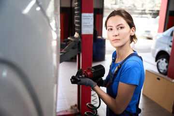 Fototapeta premium Woman auto mechanic works with a car on car lift