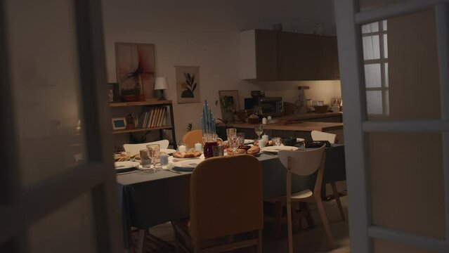 Full shot of dinner table prepared for Hanukkah celebration at Jewish family home - hanukkiah with burning candles, holy Torah book, plates with traditional foods and treats, waiting for guests