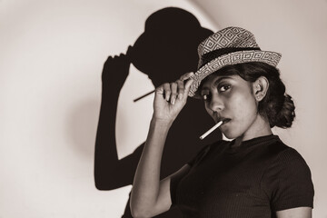 multiracial woman holding a cigarette and smoking in a vintage style photography with a cap like a...