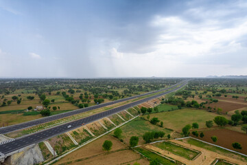 aerial drone rising over pond and green fields with delhi mumbai highway stretching off into...