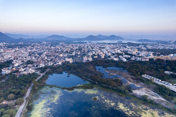 Aerial drone shot over udiapur, jaipur, kota,, cityscape with homes, houses, buildings and aravalli hills and lakes in the distance hidden in fog