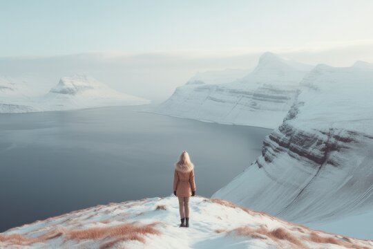 Woman on snowy mountain looking towards the ocean in the Faroe Islands