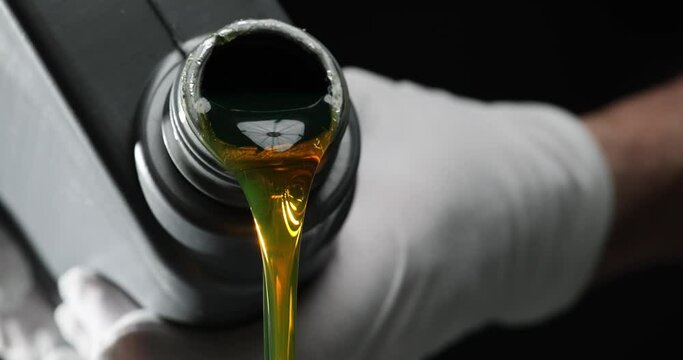 Motor oil is pouring from a canister in hand on black background. Oils and lubricants for car