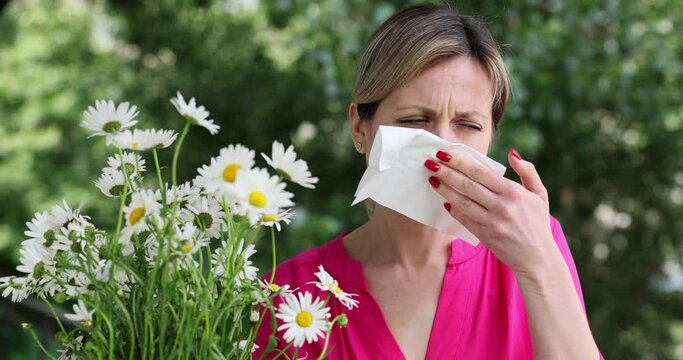Portrait of woman allergic to wild spring flowers and holding bouquet in hands. Girl blowing nose in handkerchief
