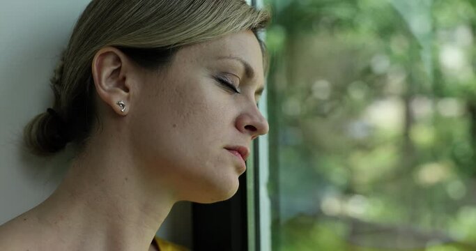 Young woman alone at home thinks about loneliness or grief and sits window and looks out into street with lonely expression. Loneliness depression and stress