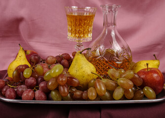 A metal tray with various fruits, a crystal decanter and a drinking glass are filled with white...