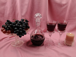 Crystal vase with black grapes, crystal decanter and crystal glasses with grape wine, on a pale pink satin background. Set of antique crystal glassware. 
