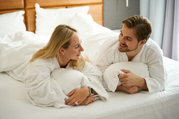 Guy and his girlfriend are talking while lying on large bed