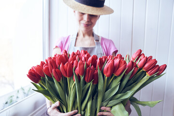 Woman holding a big bouquet of red tulips with a copy space. Gardener wearing a hat and holding beautiful flowers in the greenhouse.