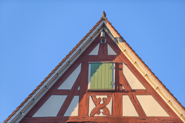 Fachwerkgiebel mit grünem Fensterladen und Taube auf Dachfirst vor blauem Himmel