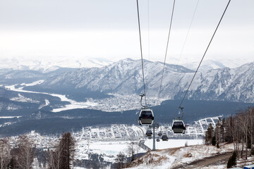 Cabin of a gondola cableway suspended on a rope where sits people with skis and snowboards high in...