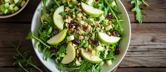 Green apple salad with rocket, oat granular, dried cranberry, and cashew nut in white dish on wooden table. Oil vinegar dressing, side dish. Two rocket leaves for decoration. - Powered by Adobe