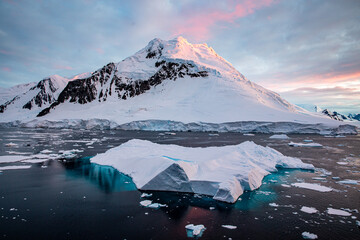 Floating iceberg with pool on the top of the iceberg with clear visible part under the water, glacier in the background and sunset sunrise sky