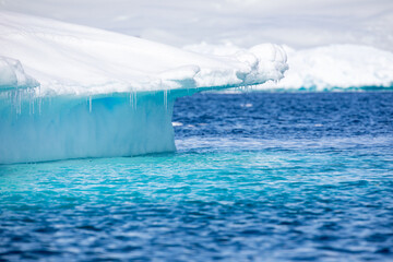 Floating iceberg with clear visible part under the water, high ice in the background and blue sky