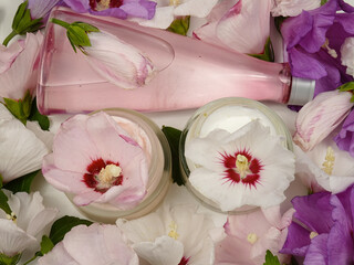 Glass jars with a cosmetic cream based on a mallow plant, a bottle of tonic on a background of...