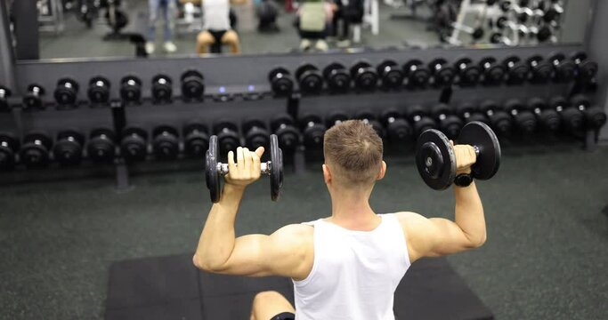 Man does lifts and holds heavy dumbbells in hands. Bodybuilder exercising arm muscles