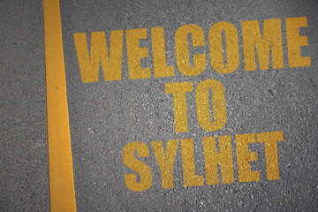 asphalt road with text welcome to Sylhet near yellow line.
