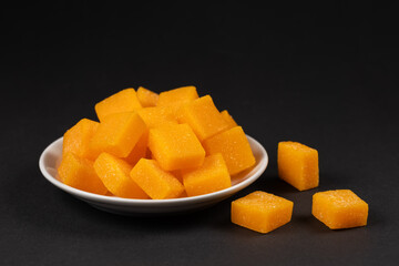 Dried and candied mango cubes on the white plate. Side view, close up, selective focus, vegan, vegetarian food concept