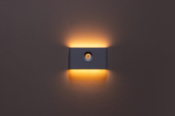 The lamp shines with warm light on the wall. Warm lighting.