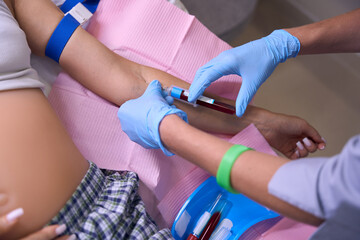 Partial image of female nurse taking blood with syringe of pregnant woman