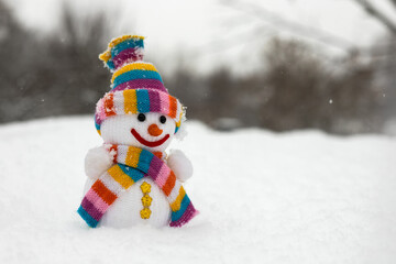 A fabric snowman in a scarf and hat stands on the snow in winter