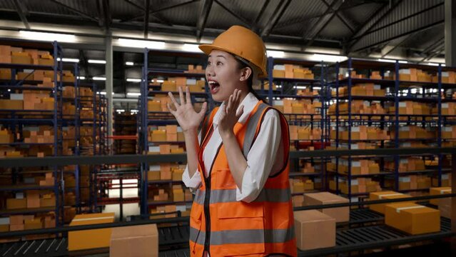 Side View Of Asian Female Engineer With Safety Helmet Standing In The Warehouse With Shelves Full Of Delivery Goods. Saying Wow In The Storage
